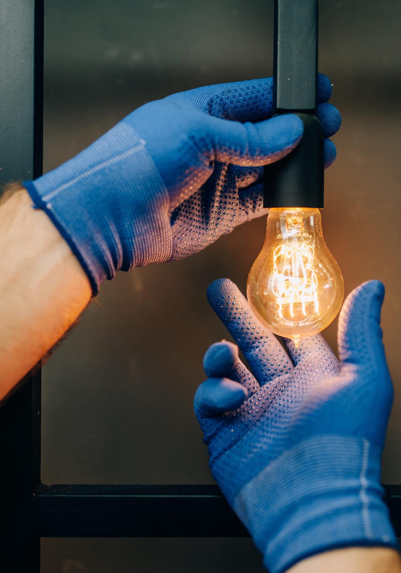 Electrician changes the light bulb, handyman Electrician in uniform replaces the light bulb, handyman. Professional worker makes repairs around the house, home repairing service
